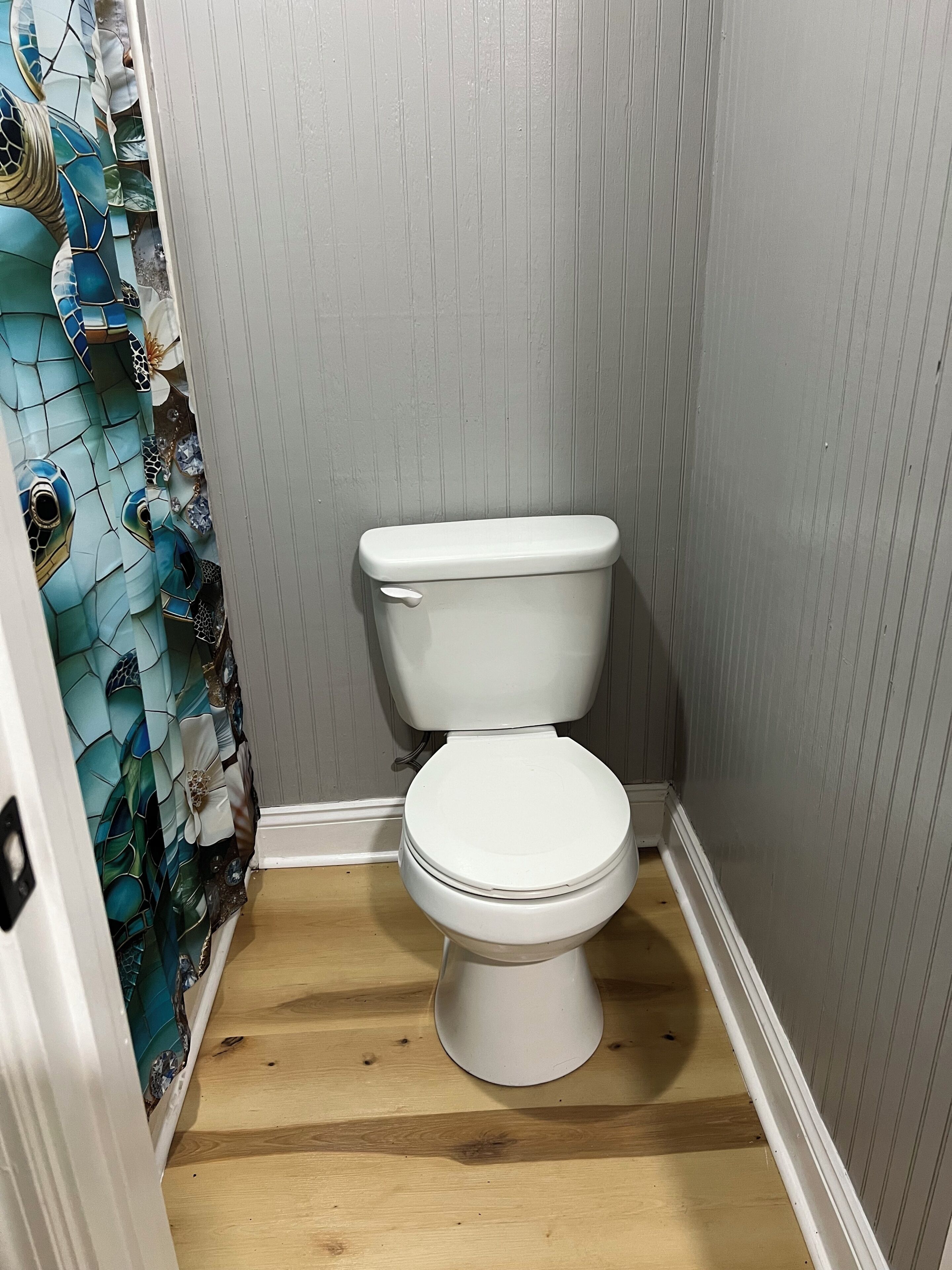 A bathroom with a white toilet, wooden flooring, and a wall with vertical paneling.