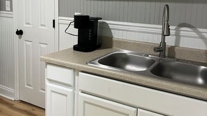 Une cuisine équipée d’un évier à deux bacs, de meubles blancs, d’une machine à café et d’un tableau accroché au-dessus de l’évier.