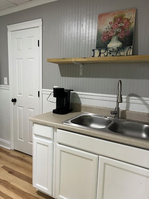 A kitchen with a double sink, white cabinets, a coffee maker, and a painting above the sink.