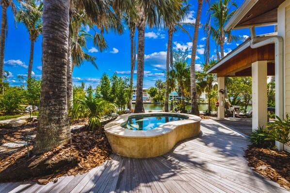 Eine Holzterrasse mit Pool, umgeben von Palmen und blauem Himmel.