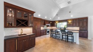 Uma cozinha com armários de madeira escura, uma ilha central com banquetas e iluminação pendente.