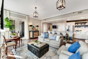 A spacious living room with a sofa, ottoman, and dining area. - "Heron Walk" Blue Mountain Beach, 30A Condo, Pool, Beach Access (Santa Rosa Beach)