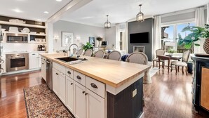 A modern kitchen with a central island, built-in appliances, and a dining area with a view. - Heron Walk, 30A Condo, Pool, Beach (Santa Rosa Beach)