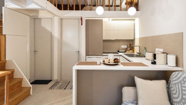 A modern kitchen with a central island, wooden staircase, and a loft area with exposed beams. - Laena Apartment by All About Paxos (Gaios)