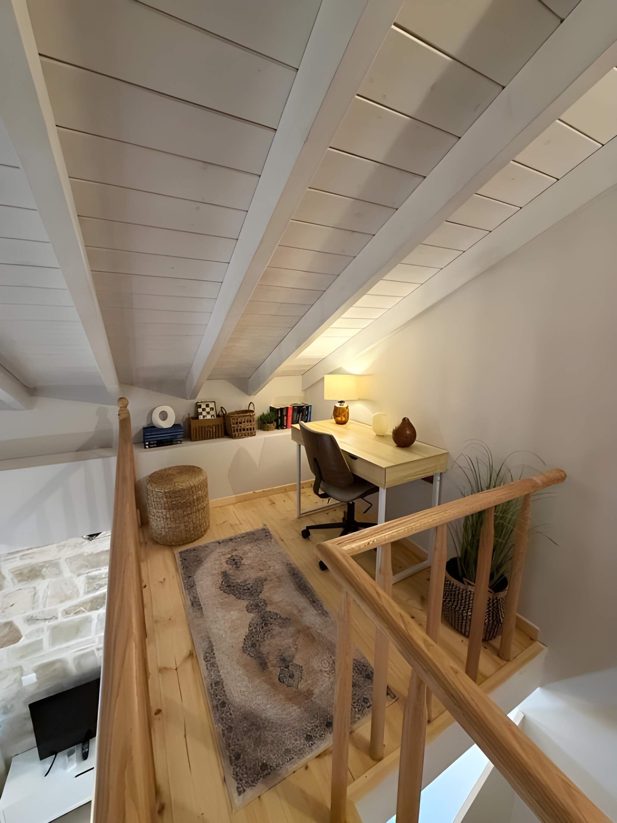 A loft bedroom with a desk, chair, and a small plant.