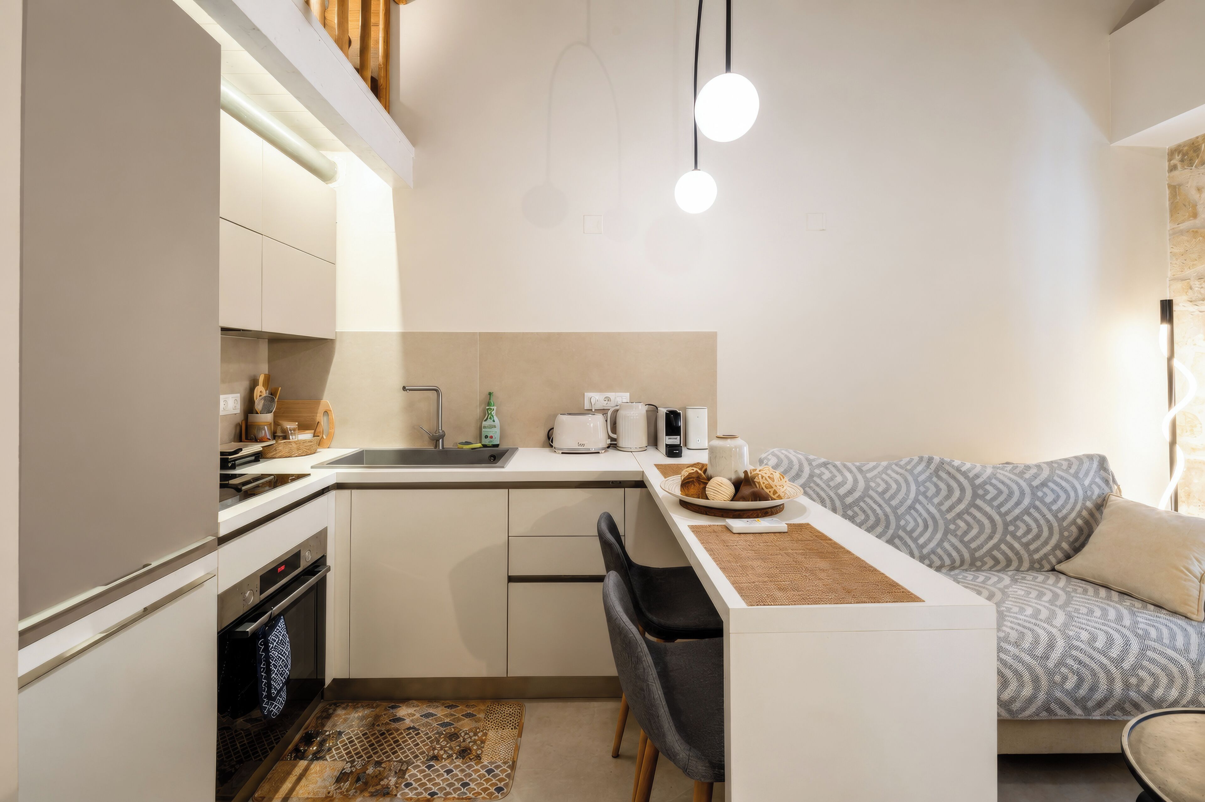 A compact kitchen with a dining area, a sofa, and a small island with a coffee maker and a kettle.