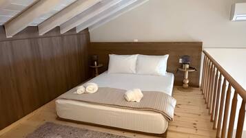 A bedroom with a wooden ceiling, a bed with white bedding, two bedside tables with lamps, and a wooden railing along the window.
