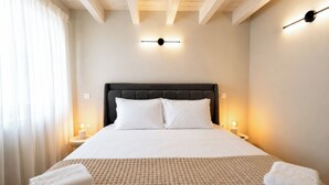 A neatly made bed with a headboard, two bedside lamps, and a window with curtains. - Laena Apartment by All About Paxos (Gaios)