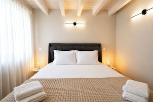 A neatly made bed with a headboard, two bedside lamps, and a window with curtains.