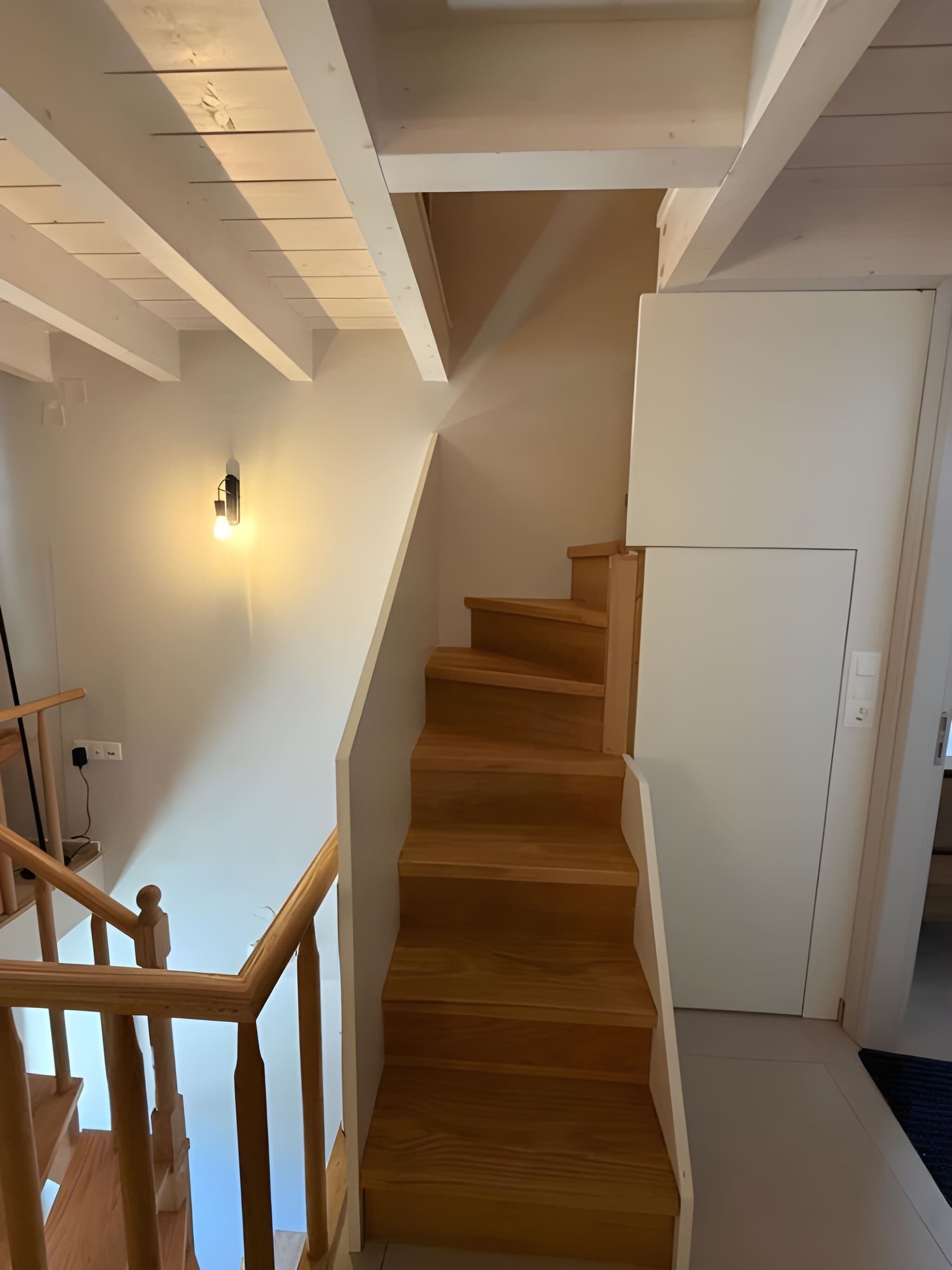 A wooden staircase with a handrail, a light fixture on the wall, and a door at the top.