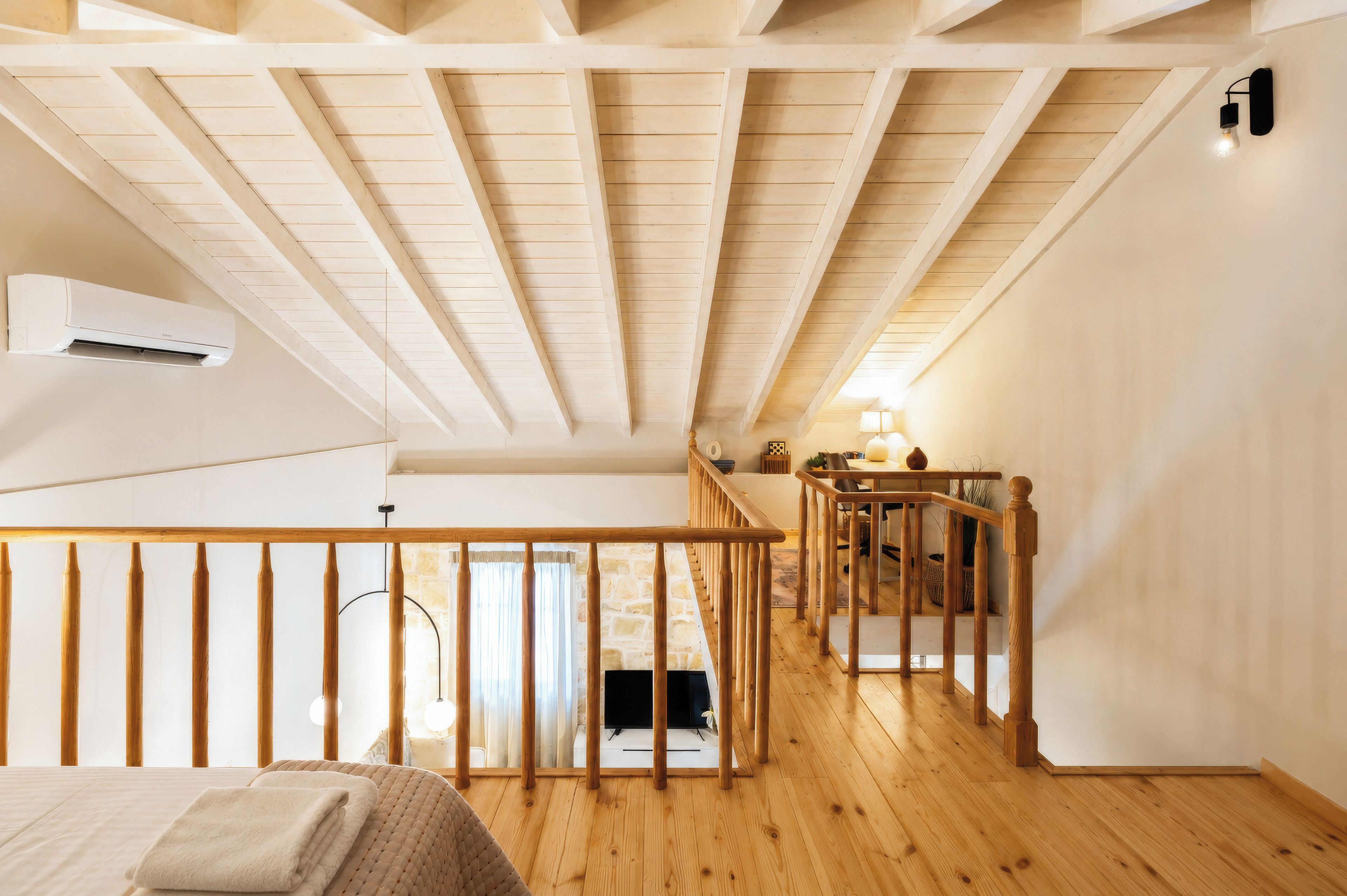 A bedroom with a wooden ceiling, a bed, a nightstand, a lamp, and a staircase leading to an upper level.