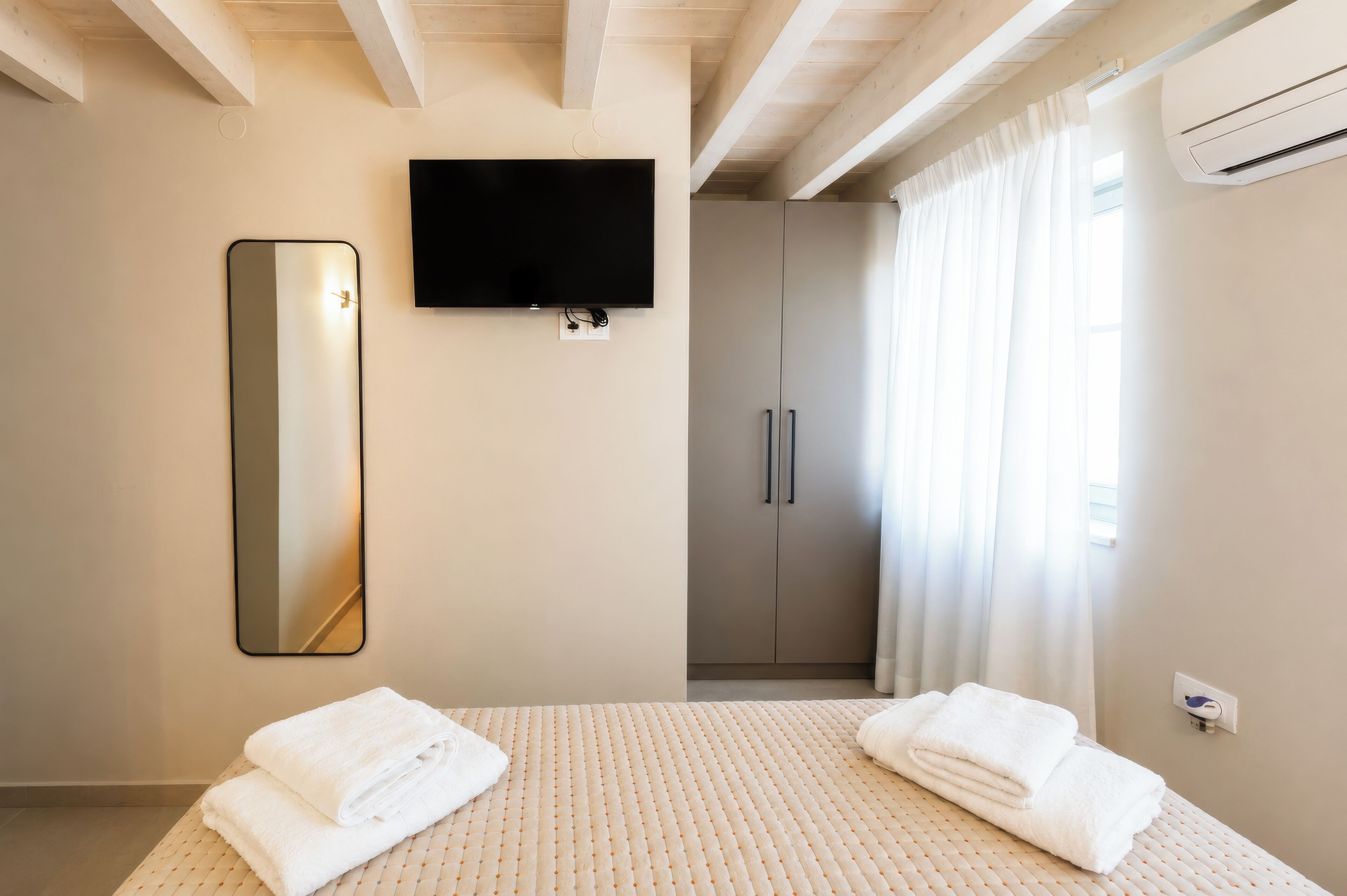 A hotel room with a bed, a TV, a wardrobe, and a mirror.