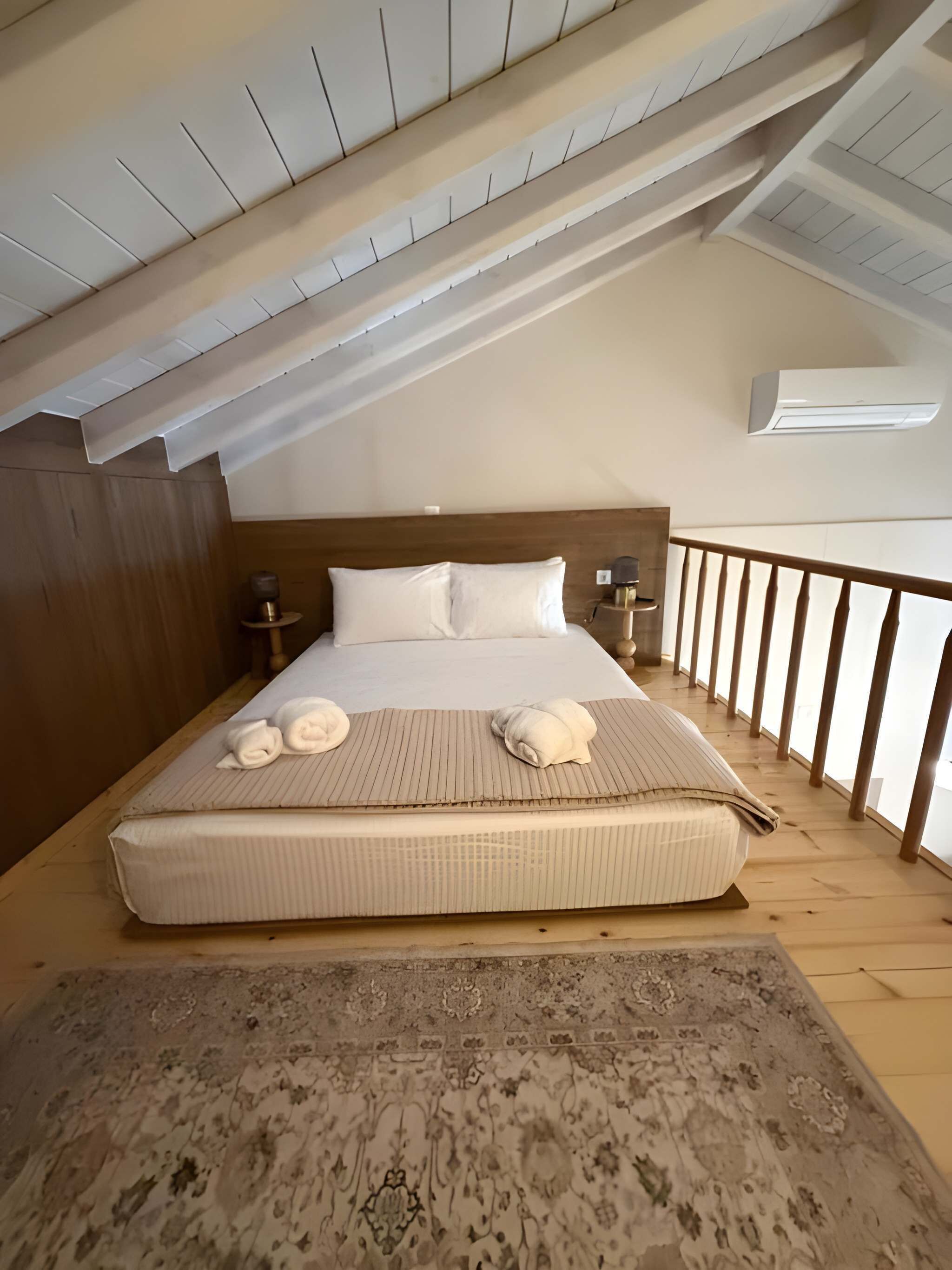 A bedroom with a large bed, wooden headboard, bedside tables, and a view of the outdoors.