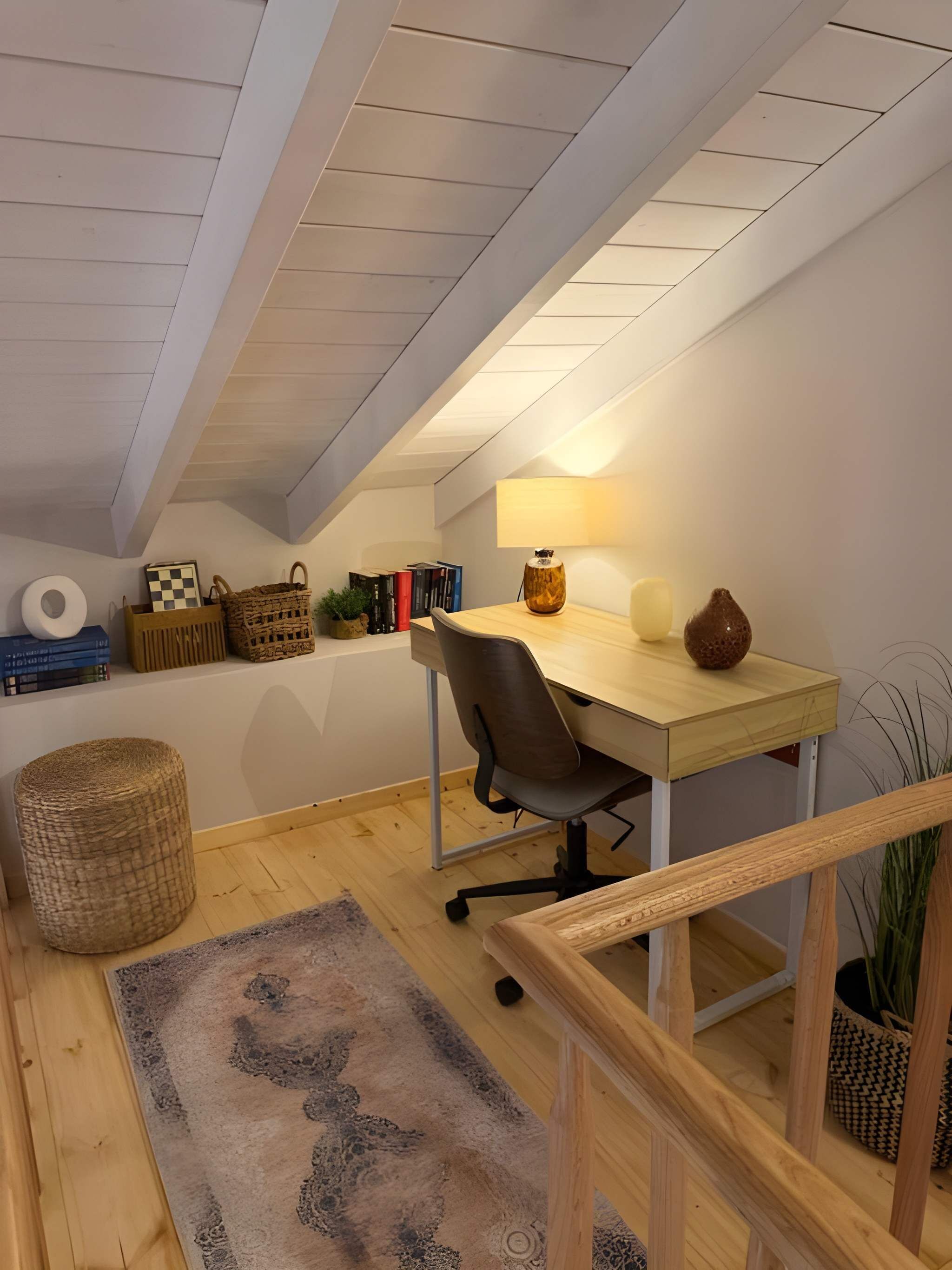 A cozy attic room with a wooden desk, a lamp, a chair, a rug, and a small plant.