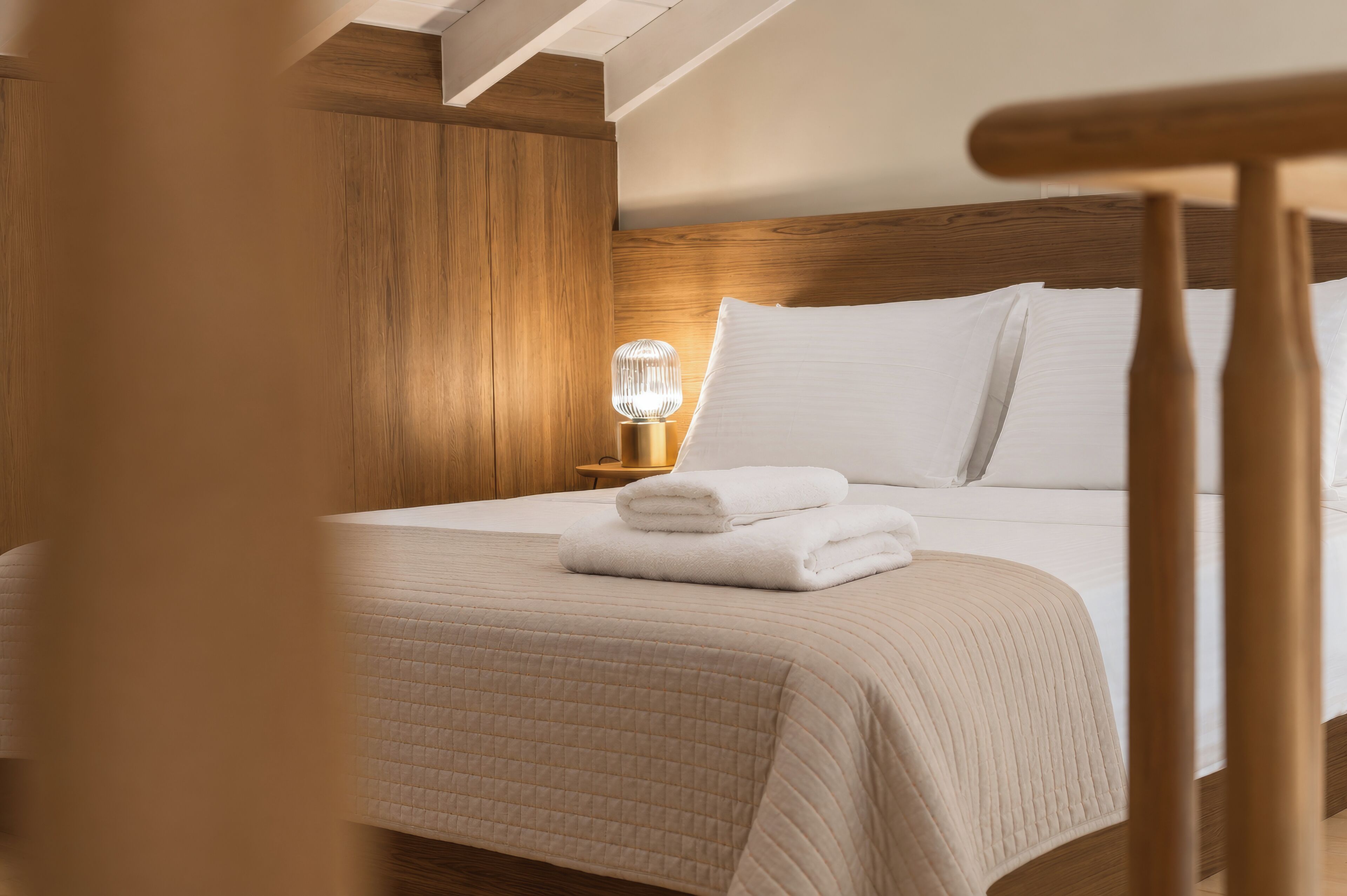 Una cama bien hecha con una colcha acolchada, una lámpara de noche y un cabecero de madera.