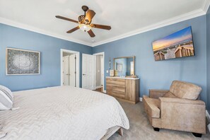 Una camera da letto con un letto, una ventola a soffitto, una cassettiera, una sedia e un quadro appeso al muro.