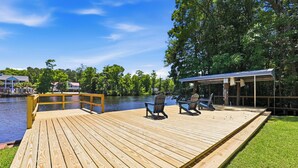 Terraza de madera con sillas y un espacio cubierto junto a un lago.