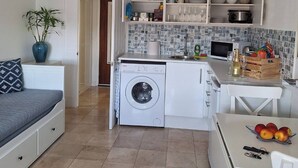 Cocina compacta con lavadora, una mesa de comedor con fruta y una cama con almohada estampada.