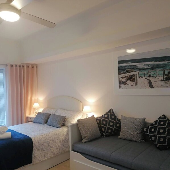 Ein Schlafzimmer mit einem Bett, Nachttischen, einer Couch, einem Deckenventilator und Meeresblick-Wandbild.