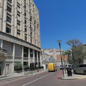 Un immeuble à plusieurs étages doté de balcons, une rue bordée de voitures garées et un fourgon jaune.