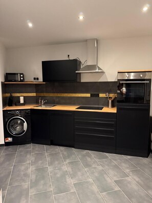 A compact kitchen with a washing machine, microwave, oven, and a large black cabinet. - RS Home CB 1 - Stylish apartment for vacation & business (Cottbus)
