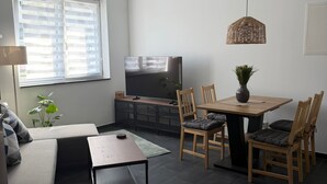 En moderne stue med sofa, spisebord med stole, fjernsyn og en hængende lampe.