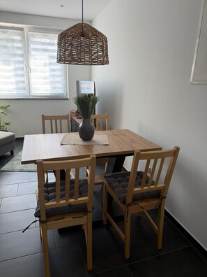 A dining area with a wooden table, four chairs, a woven pendant light, and a vase with flowers. - RS Home CB 1 - Stylish apartment for vacation & business (Cottbus)