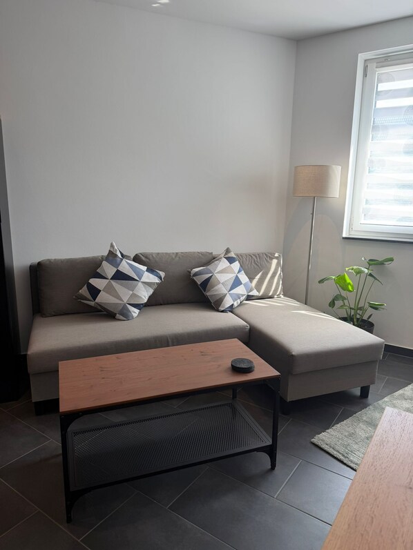 A modern living room with a sofa, two patterned cushions, a wooden coffee table, a floor lamp, and a potted plant. - RS Home CB 1 - Stylish apartment for vacation & business (Cottbus)