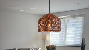 En spiseplads med et træbord, stole, en hængende lampe, en sofa med hynder, en gulvlampe og et fjernsyn.