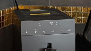 En moderne, kompakt kaffemaskine med digitalt display, vandbeholder og ledning.