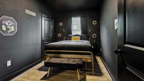 Una camera da letto con un letto, una panca, una finestra con tende e decorazioni murali tra cui un cartello con la scritta 'SAINTS' e un'immagine di un giocatore di calcio.
