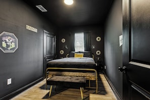 A bedroom with a bed, a bench, a window with curtains, and wall decorations including a 'SAINTS' sign and a football player image.
