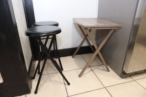 Un coin de pièce avec une porte noire, une petite table en bois et deux tabourets noirs.