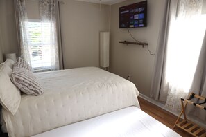 Une chambre à coucher avec un lit, un téléviseur fixé au mur et une fenêtre avec des rideaux.