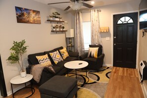 A living room with a sofa, ottoman, coffee table, and a ceiling fan. - 3-bedroom house in Tampa near USF & Bush Gardens - Fenced Yard (Tampa)