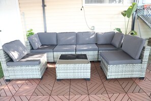 A sectional sofa with cushions, a matching ottoman, and a wicker coffee table on a tiled patio. - 3-bedroom house in Tampa near USF & Bush Gardens - Fenced Yard (Tampa)