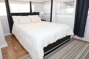 A bedroom with a large bed, a nightstand, a lamp, and a window with curtains. - 3-bedroom house in Tampa near USF & Bush Gardens - Fenced Yard (Tampa)