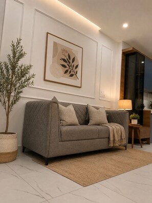 Ein modernes Wohnzimmer mit einem grauen Sofa, einem gerahmten Kunstwerk, einer Topfpflanze und einer Lampe.