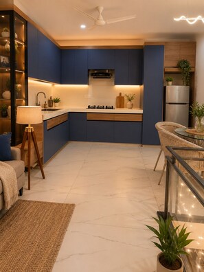 Eine moderne Küche mit Einbauherd, Kühlschrank und einer Essecke mit Glastisch und Korbstühlen.