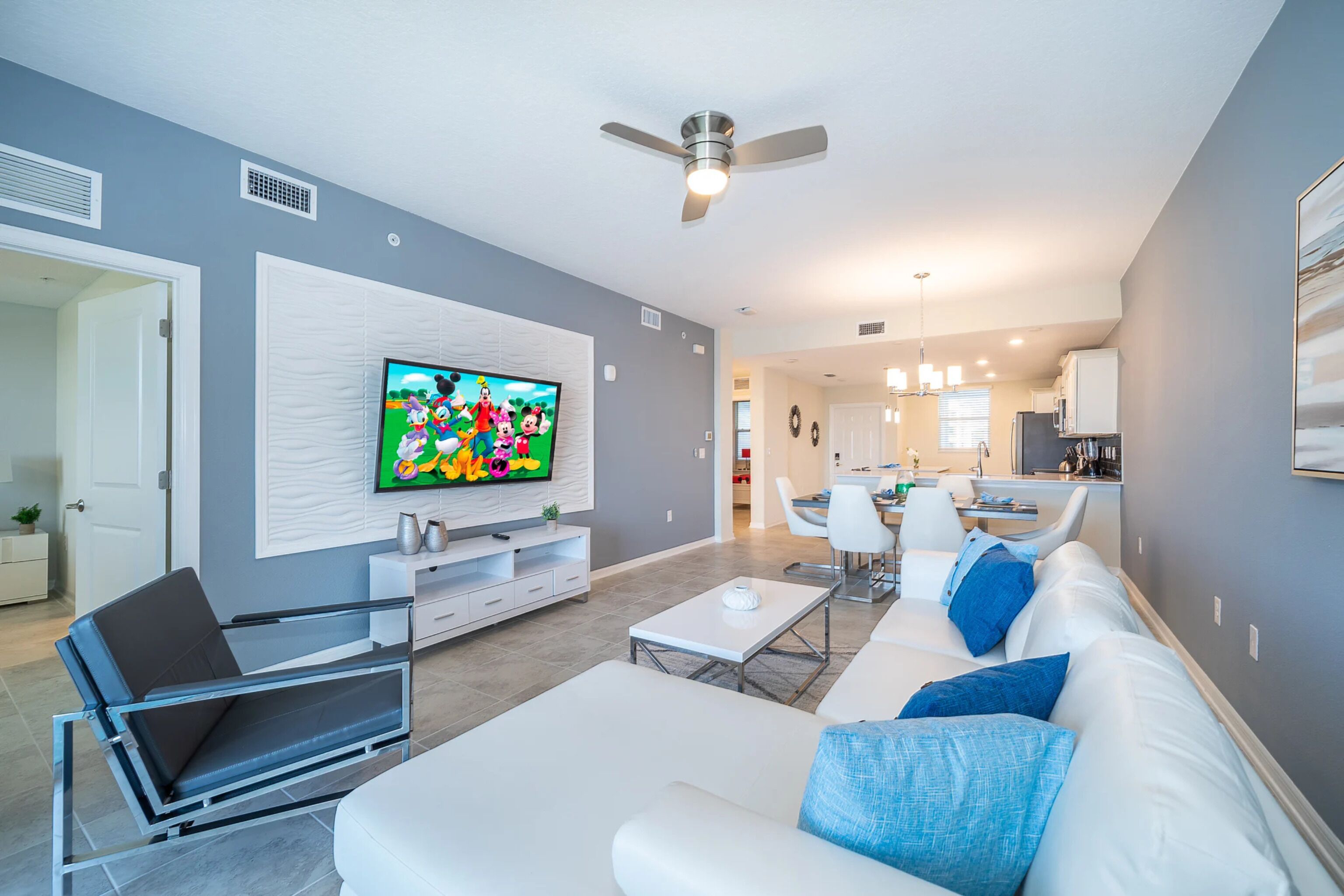 A modern living room with a flat-screen TV, a sofa, a coffee table, and a dining area with chairs.
