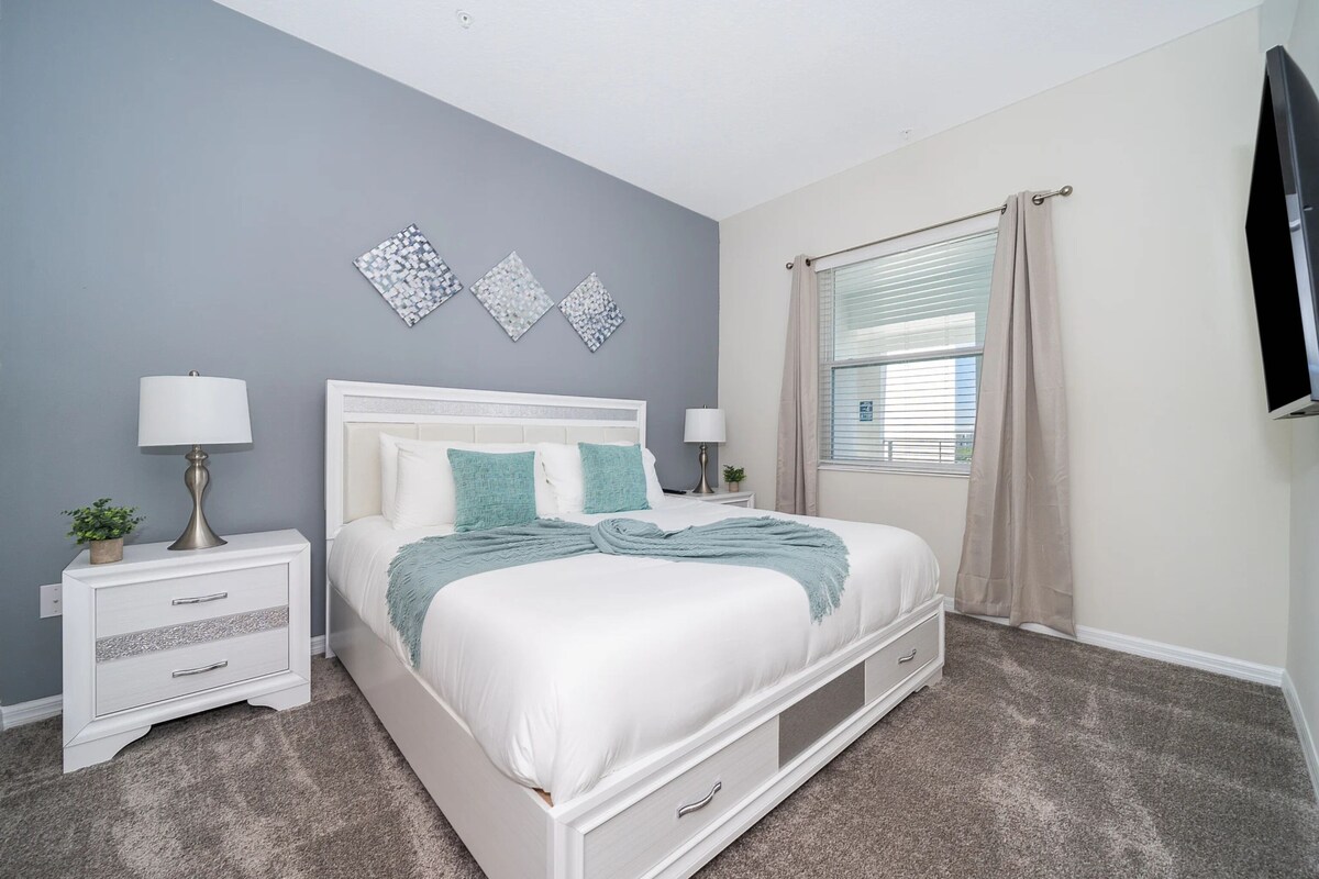 A bedroom with a bed, nightstands, a lamp, a window with curtains, and wall art.