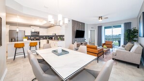 Et moderne køkken med en central ø, et spiseområde med et marmorbord og en opholdsstue med sofa og tv.