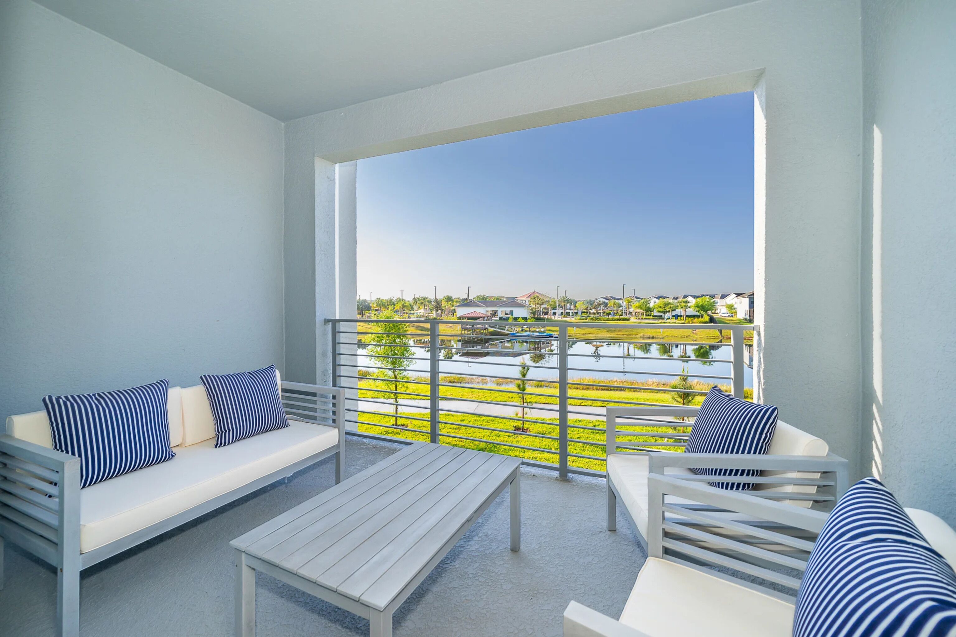 A balcony with a white sofa, a white table, and a white chair, all with blue-striped cushions.