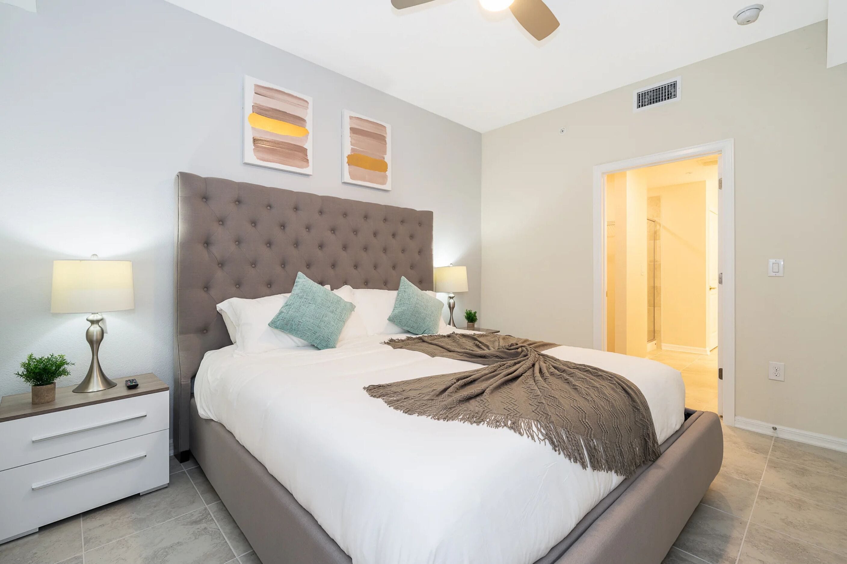 A neatly made bed with a tufted headboard, two bedside lamps, and a door leading to a bathroom.