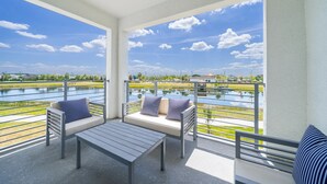 En balkon med udsigt over en sø, et bord og to sofaer med stribede puder.