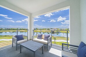 A balcony with a view of a lake, a table, and two sofas with striped pillows. - AEA - 3141 Paradox Circle FL (Kissimmee)