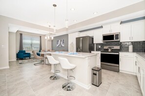 A modern kitchen with white cabinets, stainless steel appliances, and a central island with bar stools. - AEA - 3141 Paradox Circle FL (Kissimmee)