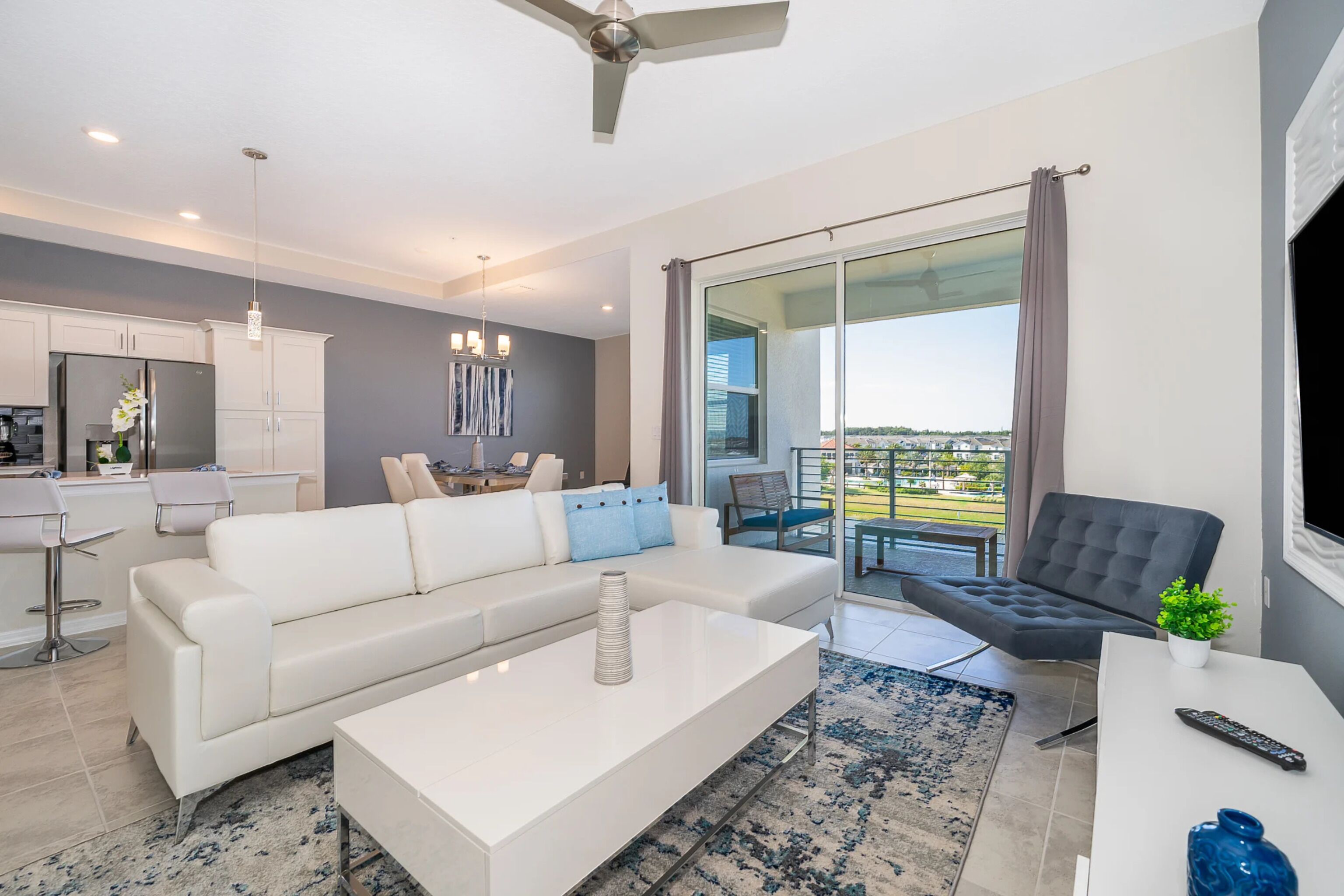 Un salon moderne avec un canapé blanc, une table basse, un fauteuil foncé et un balcon offrant une vue dégagée.
