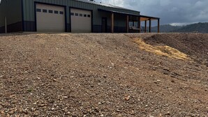 A building with multiple garage doors, a covered outdoor seating area, and a gravel driveway. - Mountain Top Sunsets on 12 secluded acres!  Brand new house finished in 2026 (Mena)