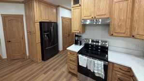 A kitchen with wooden cabinets, a black refrigerator, a stove, and a coffee maker. - Mountain Top Sunsets on 12 secluded acres!  Brand new house finished in 2026 (Mena)